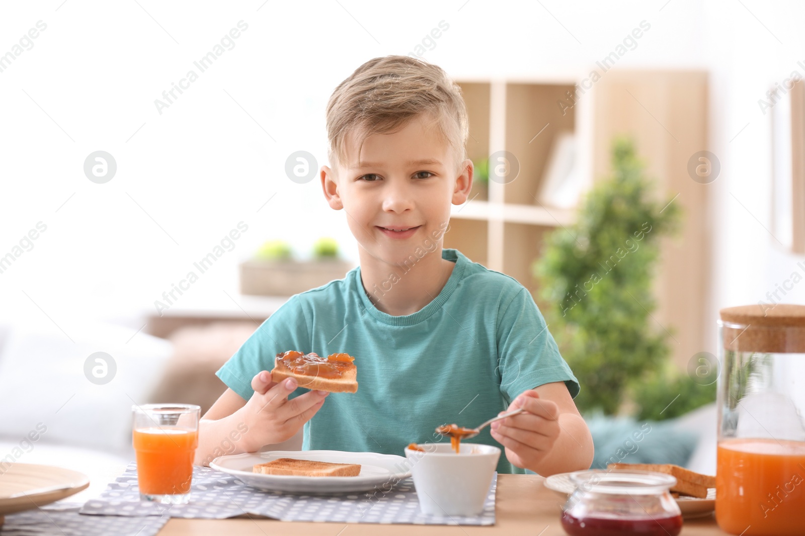 Photo of Cute little boy spreading jam onto tasty toasted bread at table