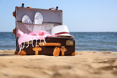 Open suitcase with stylish beach accessories on sand near sea. Space for text