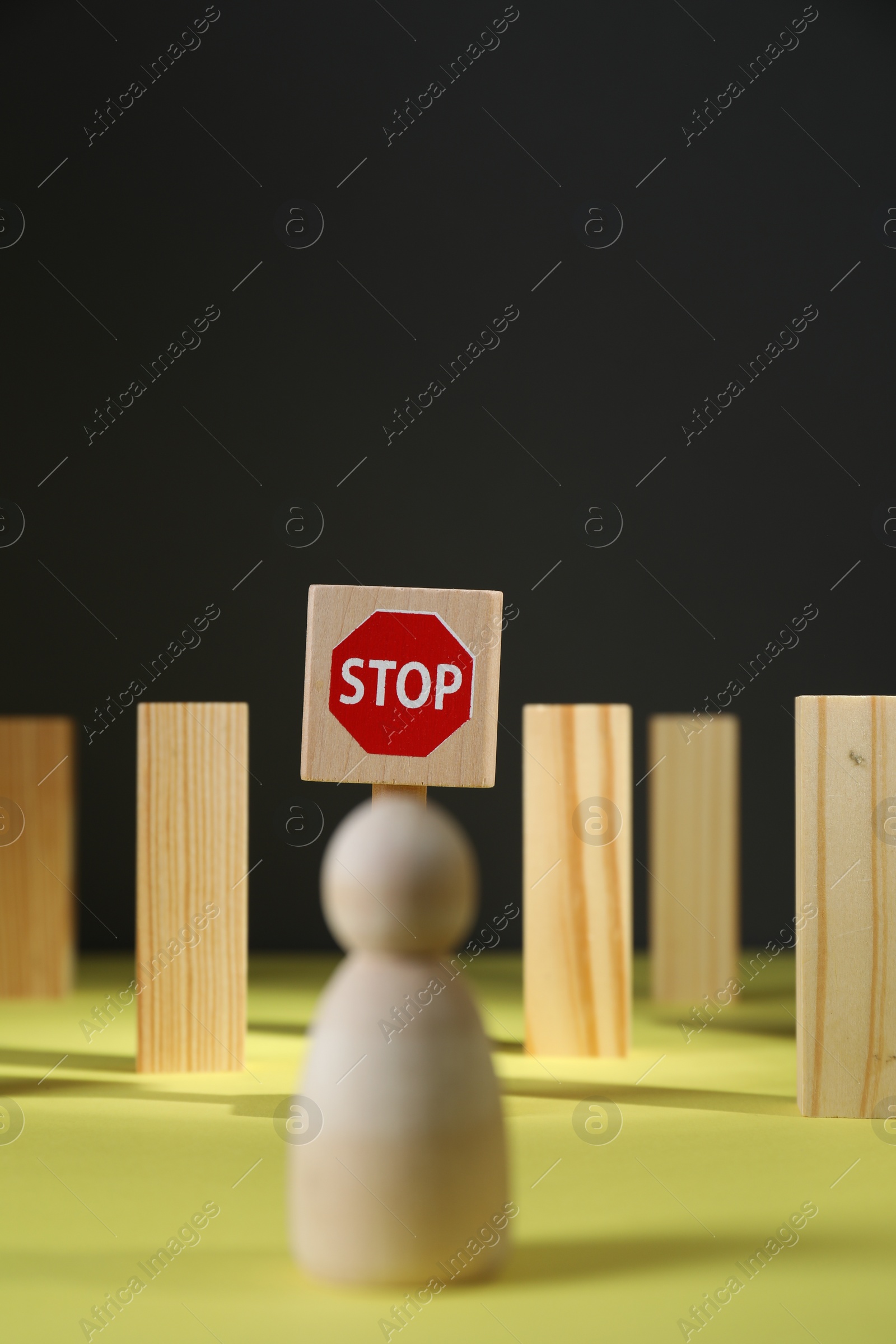 Photo of Road Stop sign and blocks as barriers blocking way for wooden human figure on yellow surface. Development through obstacles overcoming