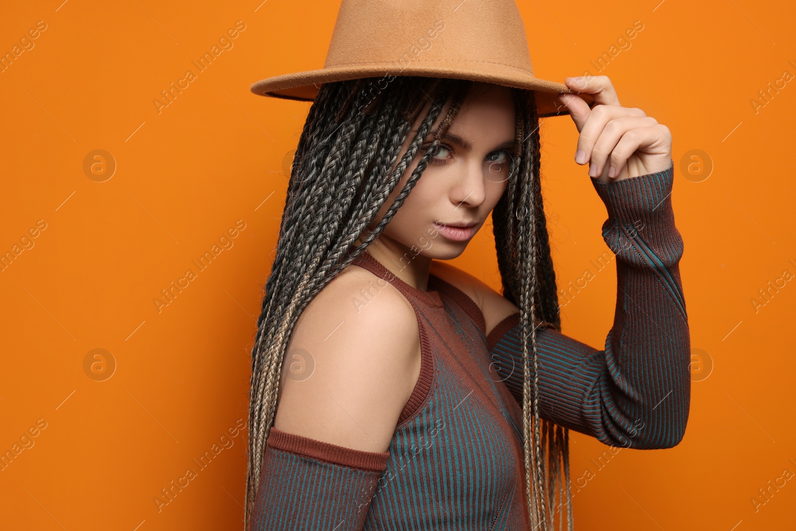 Photo of Beautiful woman with long african braids and hat on orange background, space for text