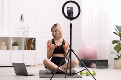 Smiling sports blogger working out with dumbbells while streaming online fitness lesson at home