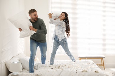 Happy young couple having fun pillow fight in bedroom