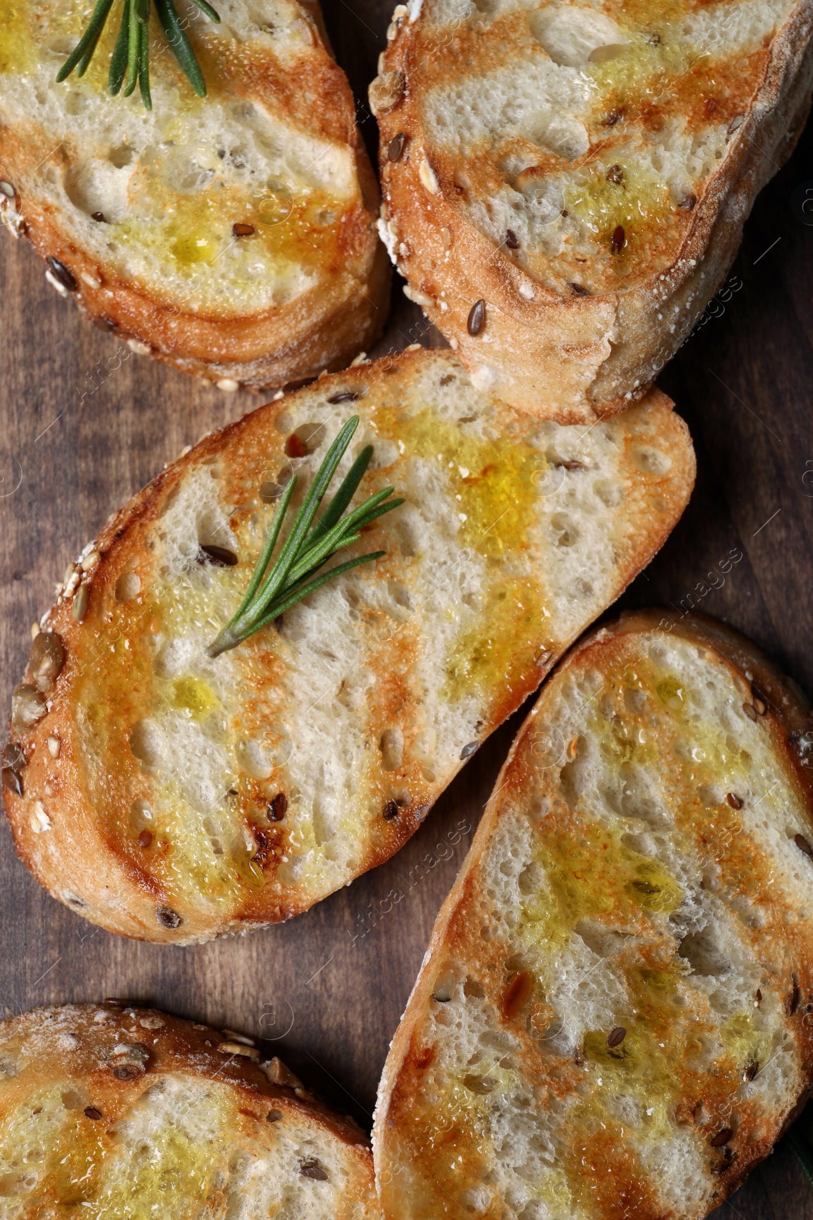 Photo of Tasty bruschettas with oil and rosemary on wooden table, closeup