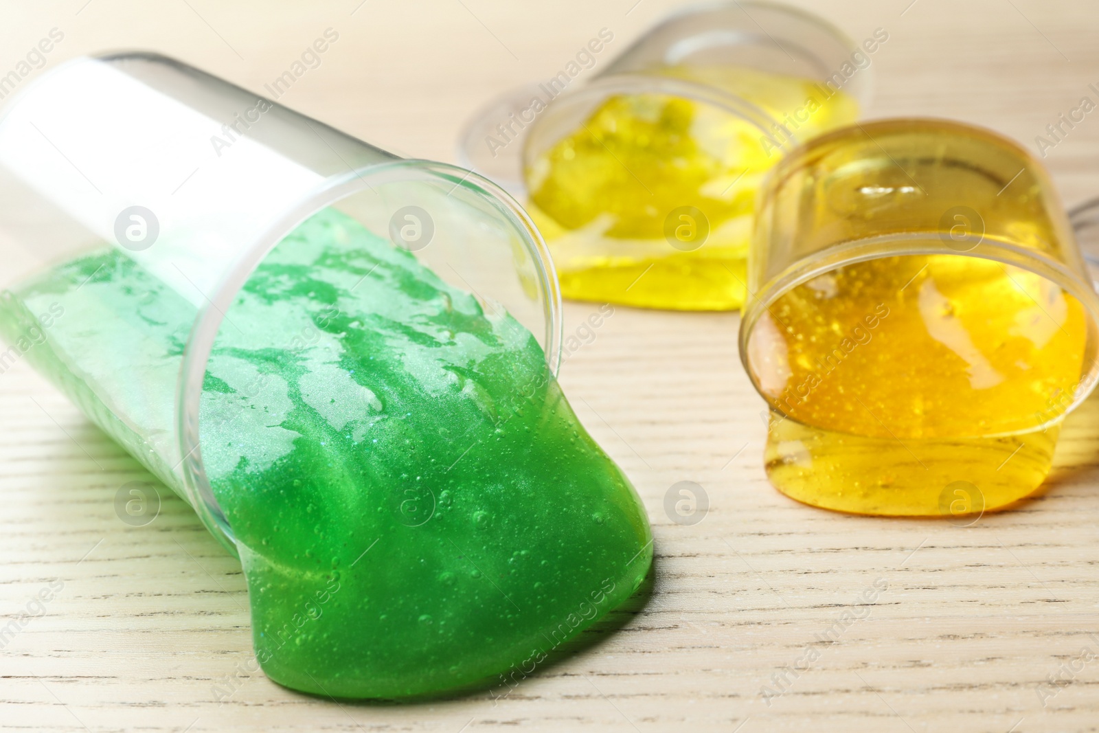 Photo of Overturned plastic containers with bright slimes on wooden background, closeup