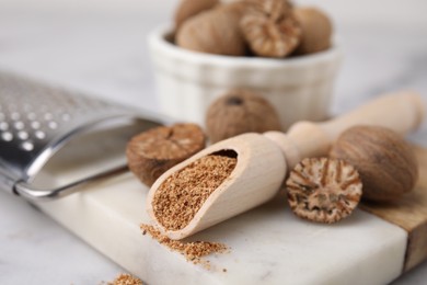 Photo of Scoop with grated nutmeg, seeds and grater on white table, closeup