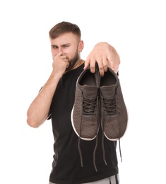 Photo of Young man feeling bad smell from shoes on white background. Air freshener