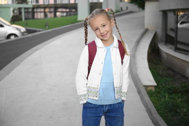 Photo of Cute little girl with backpack on city street. Space for text