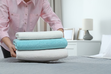 Woman putting stack of clean towels on bed. Space for text