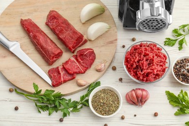 Meat grinder, beef, onion, garlic, parsley and spices on white wooden table, above view