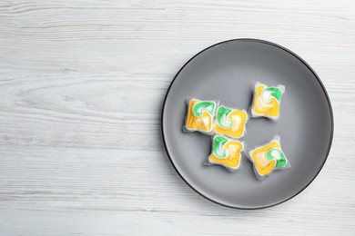 Photo of Plate with many dishwasher detergent pods on white wooden table, top view. Space for text