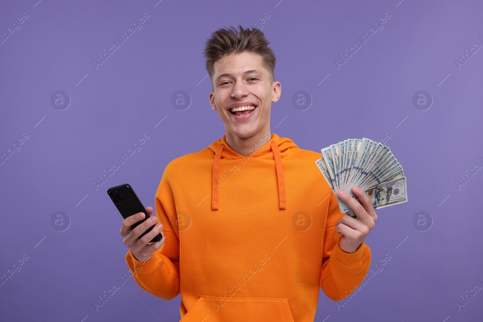 Photo of Happy man with money and smartphone on purple background