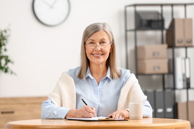 Photo of Smiling senior woman signing Last Will and Testament at table indoors