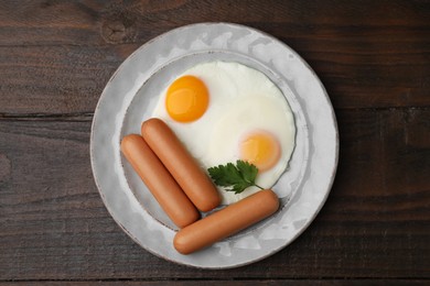 Delicious boiled sausages, fried eggs and parsley on wooden table, top view