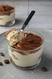 Delicious tiramisu in glass, coffee beans and spoon on table, closeup