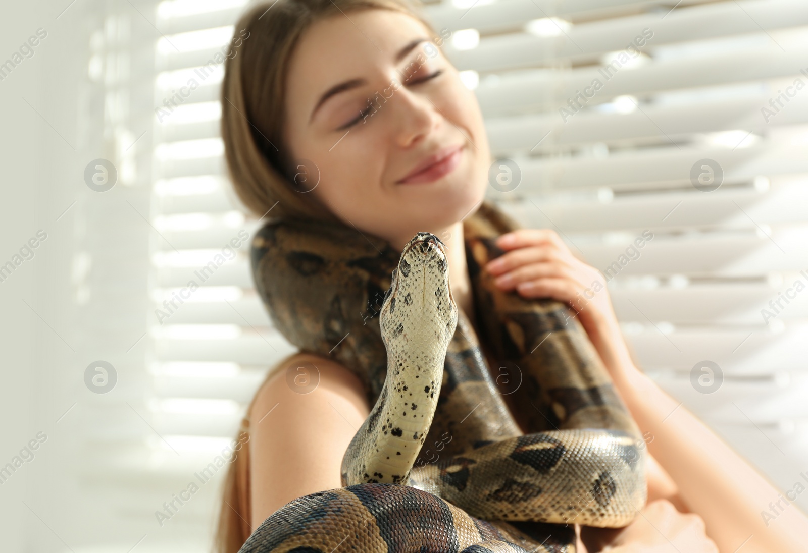 Photo of Young woman with boa constrictor at home. Exotic pet