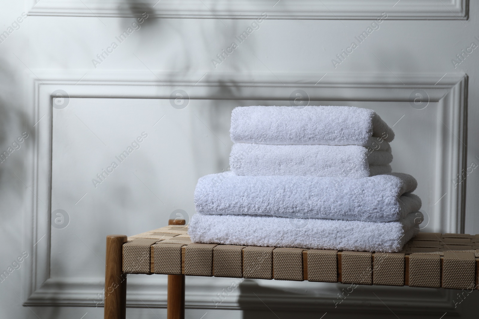 Photo of Stacked terry towels on wicker bench indoors, space for text