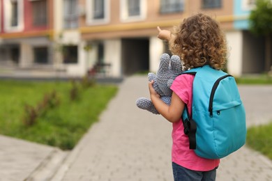 Photo of Little girl with toy walking to kindergarten outdoors, back view. Space for text