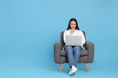 Photo of Young woman working with laptop in armchair on light blue background. Space for text