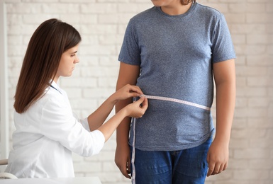 Female doctor measuring overweight boy in clinic