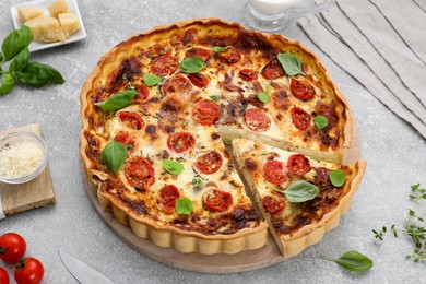 Cut delicious homemade quiche with prosciutto and ingredients on light grey table, above view