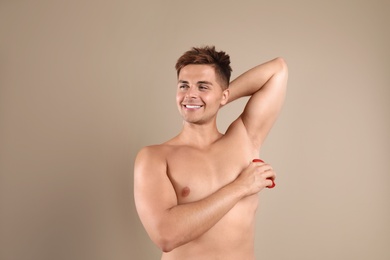 Young man applying deodorant to armpit on beige background