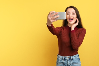 Photo of Attractive young woman taking selfie with phone on color background