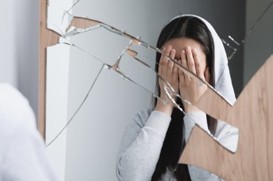 Photo of Woman covering face with hands near broken mirror. Mental problems