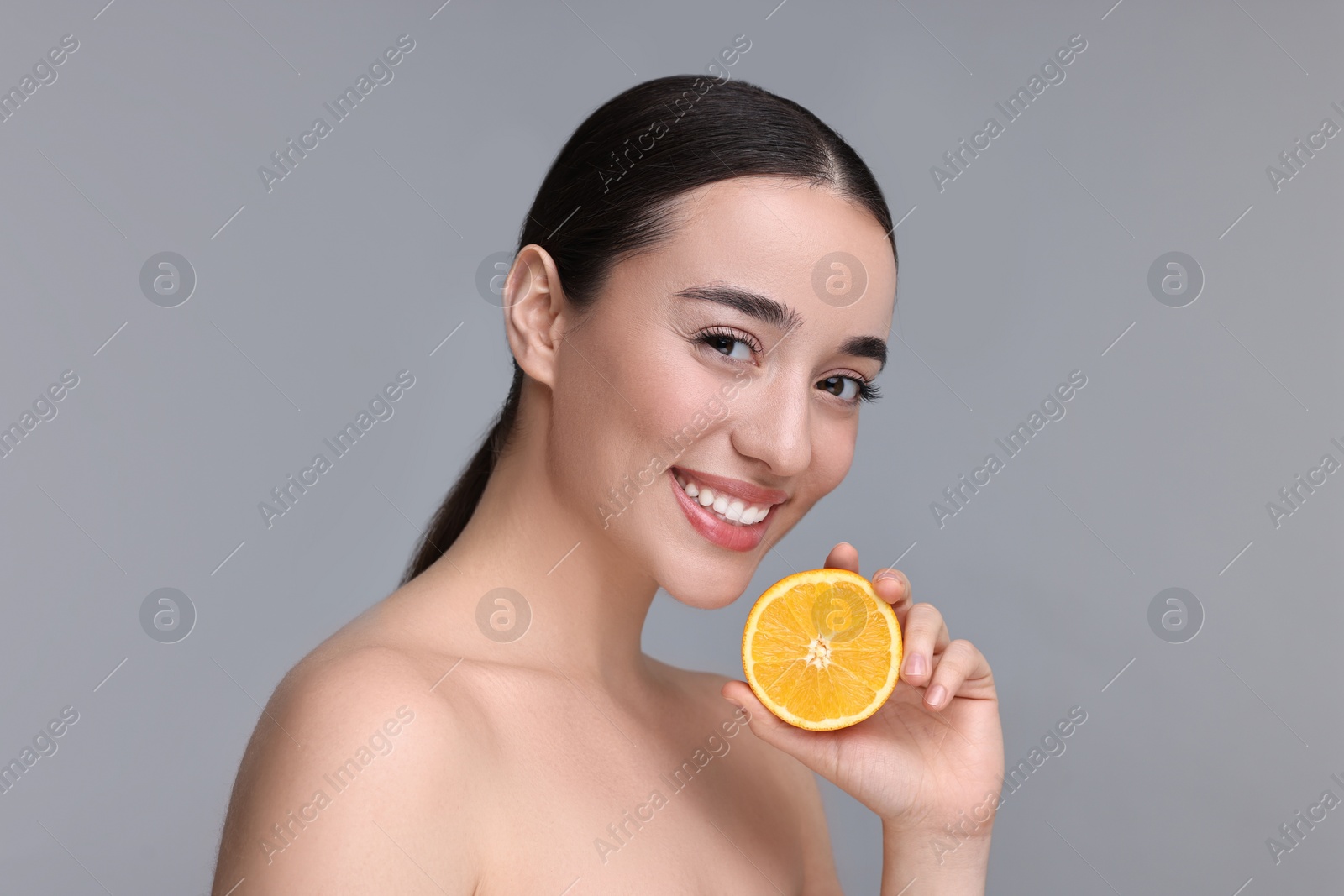 Photo of Beautiful young woman with piece of orange on grey background