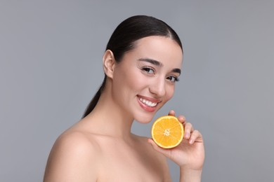 Beautiful young woman with piece of orange on grey background