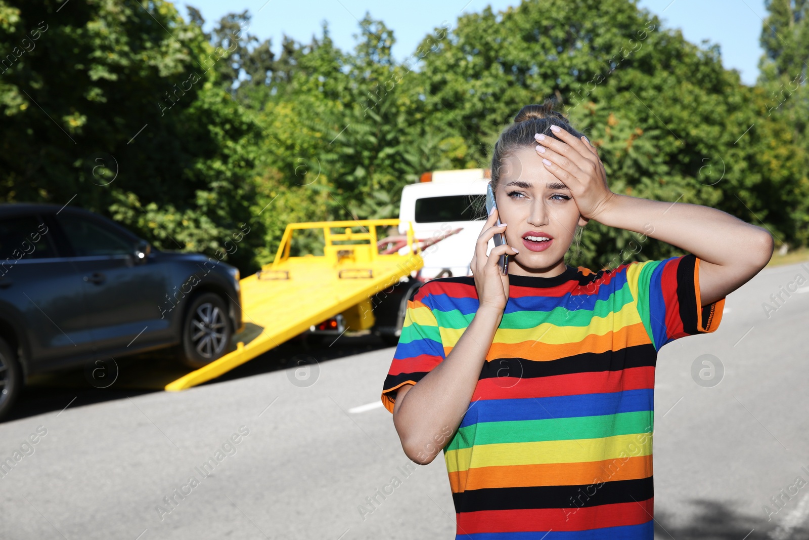 Photo of Woman talking on phone near broken car and tow truck outdoors