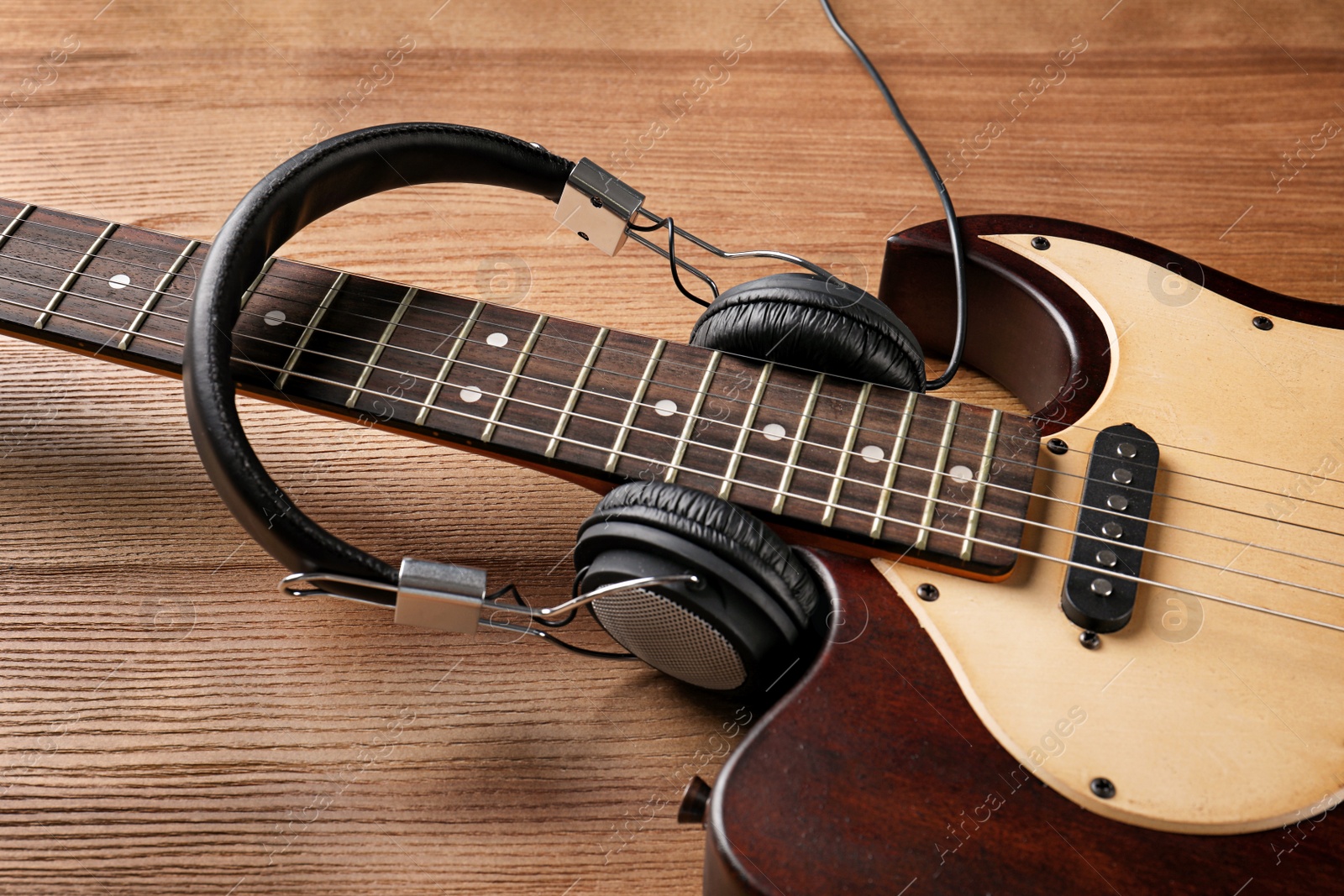 Photo of Modern electric guitar with headphones on wooden background. Musical instrument