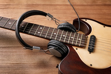 Photo of Modern electric guitar with headphones on wooden background. Musical instrument