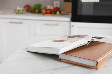 Photo of Recipe books on white marble table in kitchen, closeup. Space for text