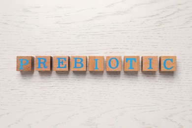 Photo of Wooden cubes with word Prebiotic on white table, flat lay