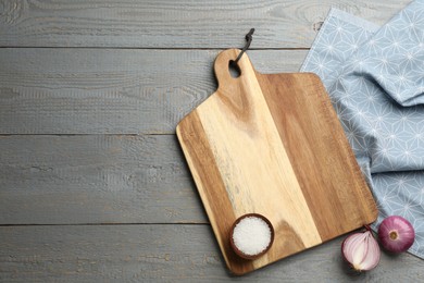 Photo of Cutting board, onion and salt on grey wooden table, flat lay with space for text. Cooking utensil