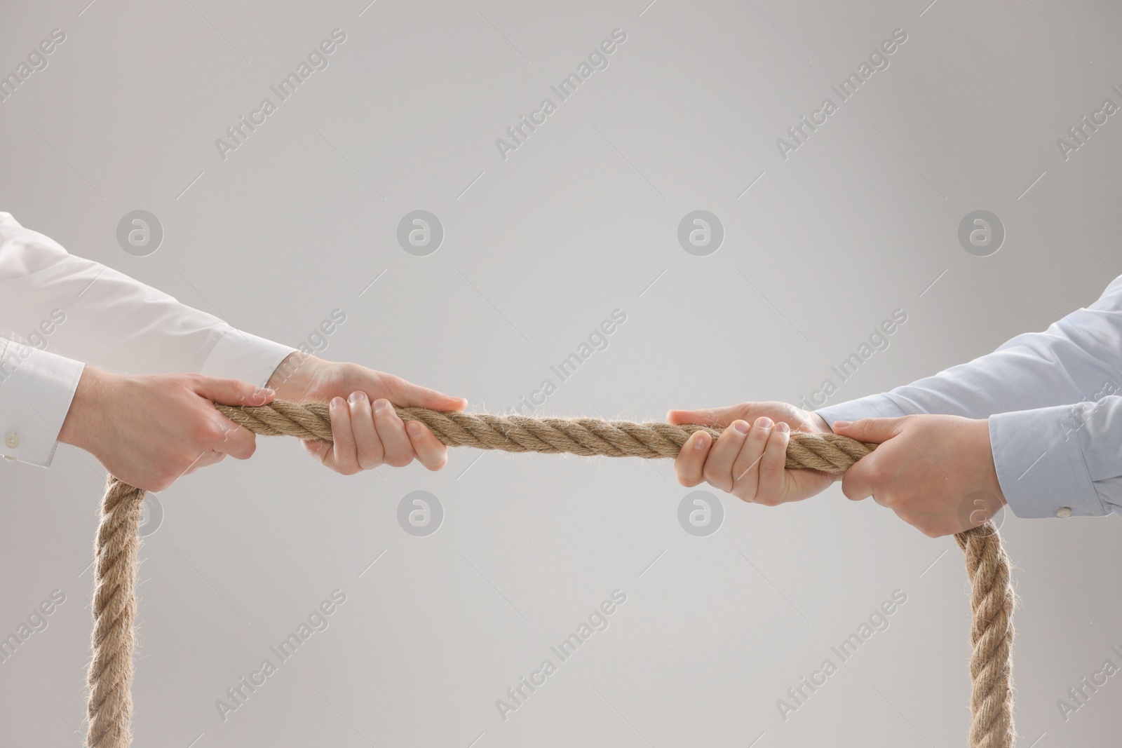 Photo of Dispute concept. Men pulling rope on light grey background, closeup