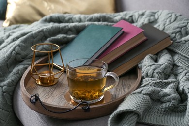 Photo of Stylish tray with different interior elements and tea on sofa