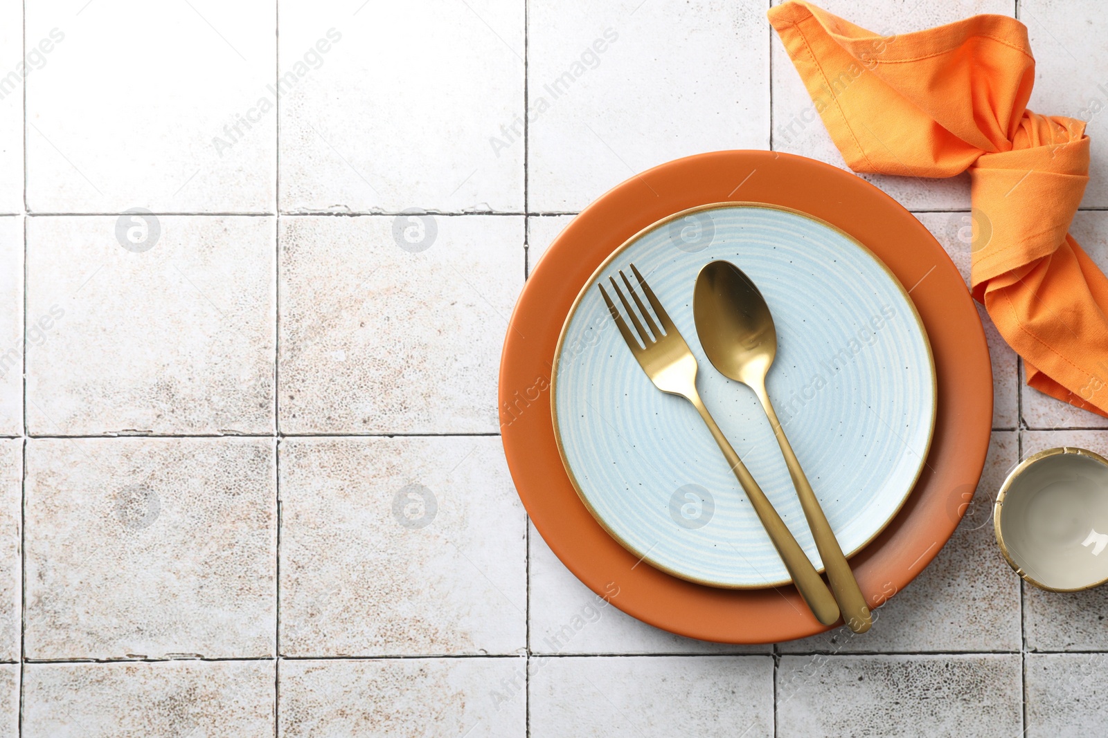 Photo of Stylish setting with cutlery, napkin and plates on light tiled table, top view. Space for text