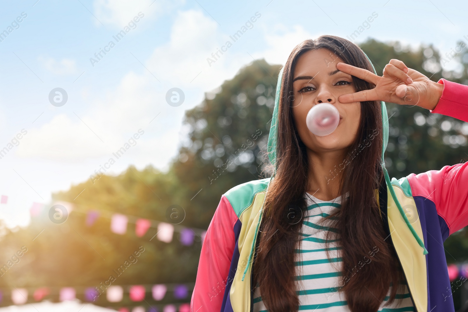 Photo of Beautiful young woman blowing chewing gum and showing peace gesture outdoors, space for text