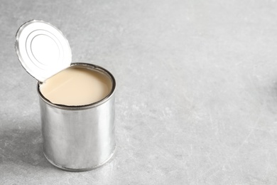 Tin can with condensed milk on grey background, space for text. Dairy product