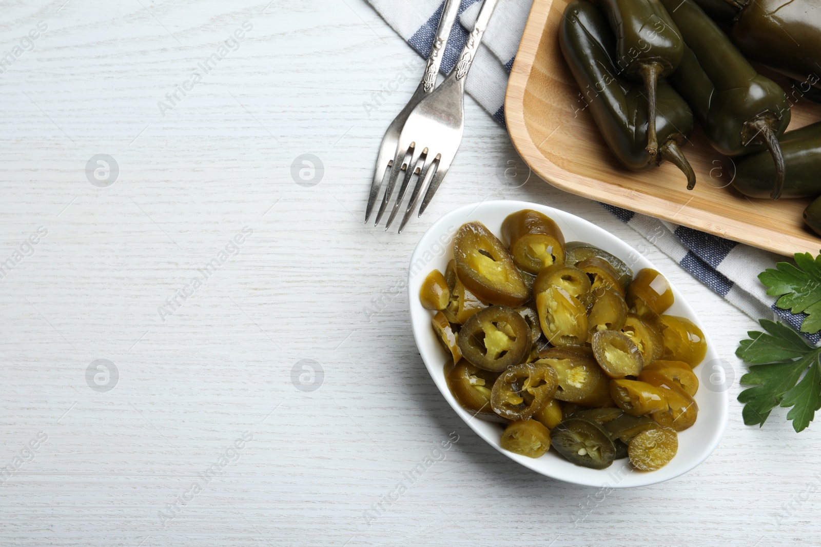 Photo of Bowl with slices of pickled green jalapeno peppers on white wooden table, flat lay. Space for text