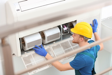 Photo of Professional technician maintaining modern air conditioner indoors