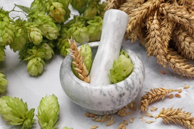 Photo of Mortar with pestle, fresh hops and ears of wheat on light grey marble table, closeup
