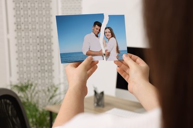Photo of Woman holding torn photo in room, closeup. Divorce concept