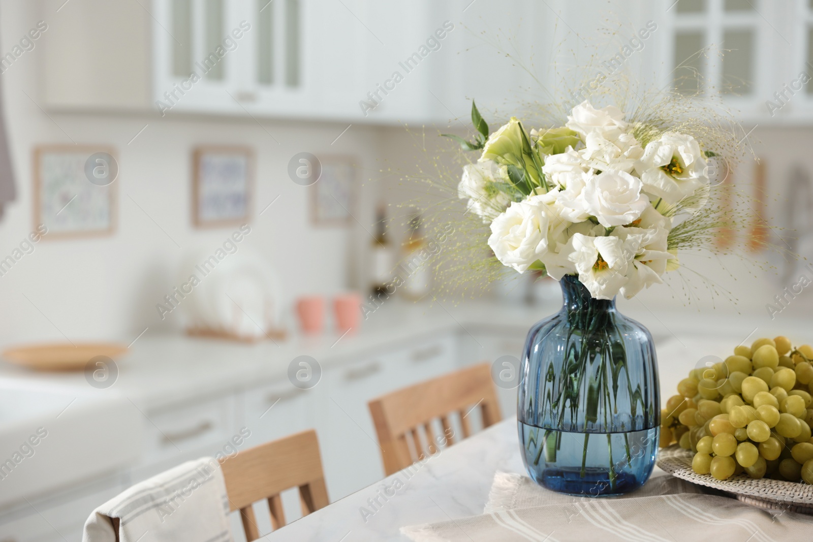 Photo of Bouquet of beautiful eustoma flowers and grapes on white table in kitchen. Interior design