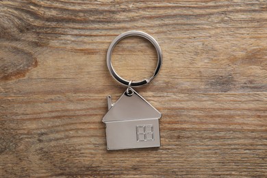 Metal keychain in shape of house on wooden table, top view