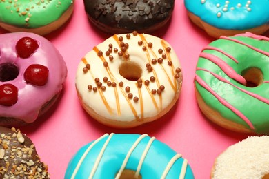 Different delicious glazed doughnuts on pink background, closeup