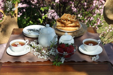 Photo of Beautiful spring flowers, freshly baked waffles and ripe strawberries on table served for tea drinking in garden