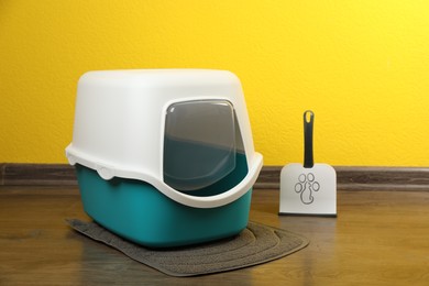 Photo of Cat litter box and scoop on floor near yellow wall