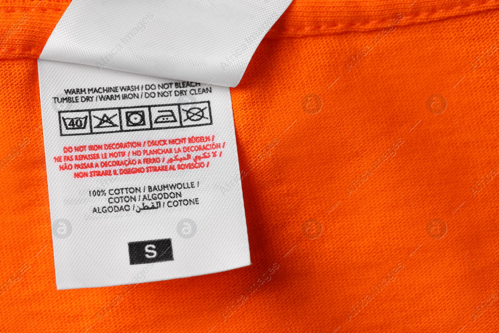 Photo of Clothing labels on orange garment, top view. Space for text